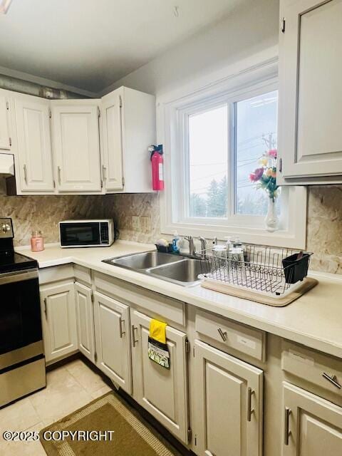 kitchen featuring a sink, stainless steel range with electric stovetop, decorative backsplash, and light countertops