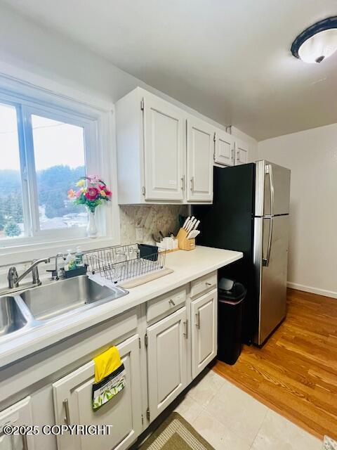 kitchen with decorative backsplash, white cabinets, freestanding refrigerator, light countertops, and a sink