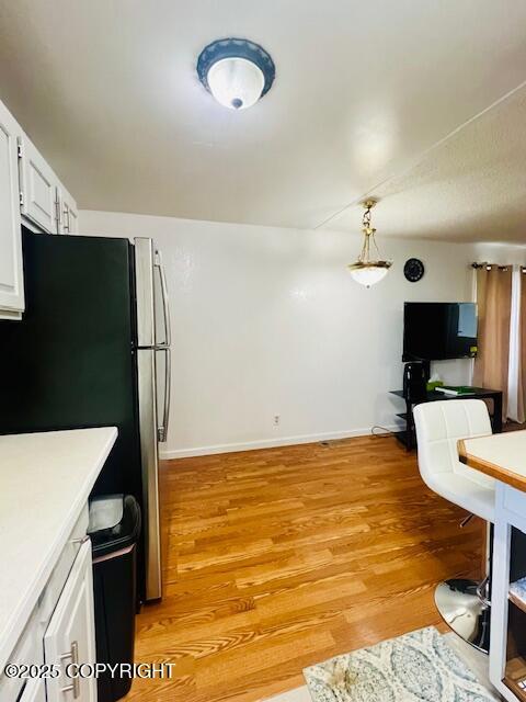 kitchen with light wood-type flooring, white cabinetry, light countertops, and freestanding refrigerator