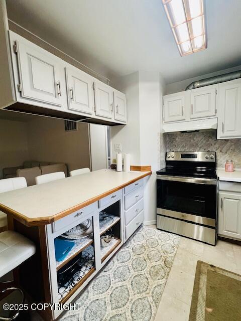 kitchen with tasteful backsplash, light countertops, white cabinets, stainless steel range with electric stovetop, and under cabinet range hood