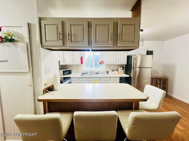 kitchen featuring tasteful backsplash, light countertops, freestanding refrigerator, a sink, and a kitchen bar