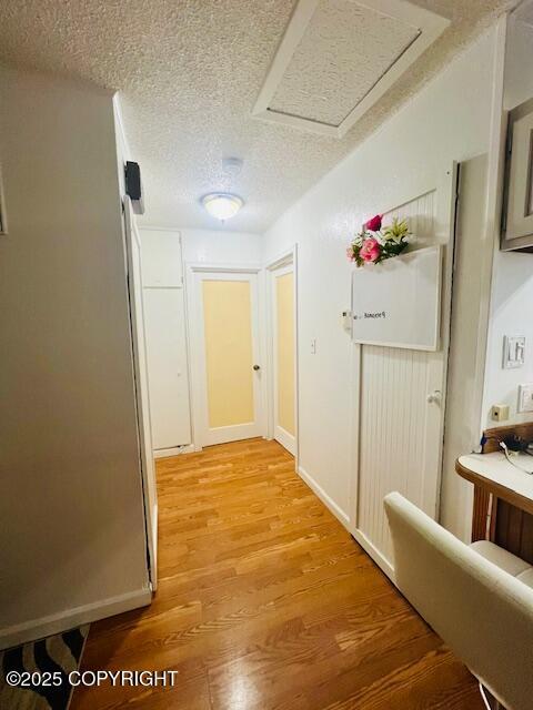 corridor featuring attic access, light wood-type flooring, and a textured ceiling