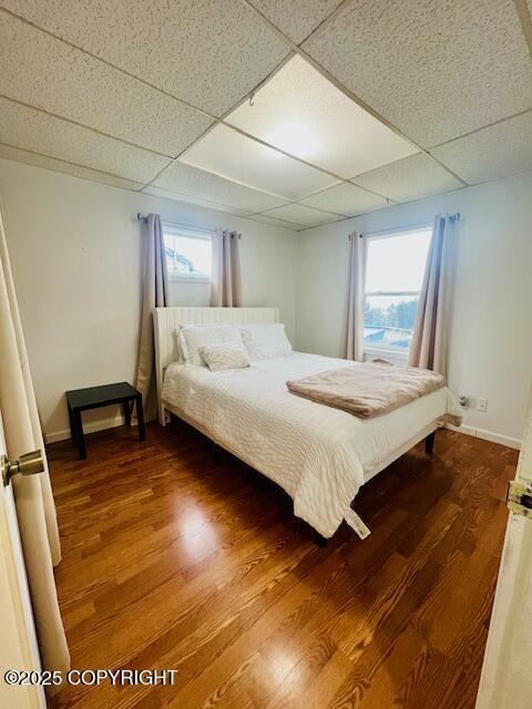 unfurnished bedroom featuring multiple windows, a drop ceiling, wood finished floors, and baseboards