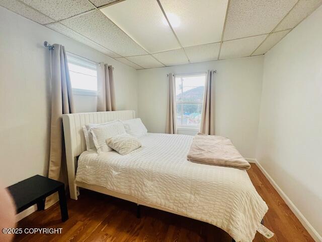 bedroom with a paneled ceiling, baseboards, and wood finished floors