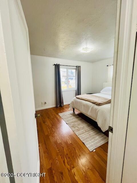 bedroom with a textured ceiling, wood finished floors, and baseboards