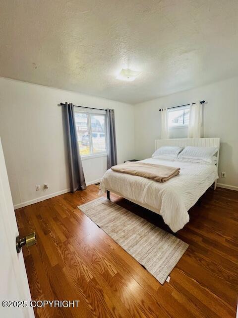 bedroom with a textured ceiling, wood finished floors, and baseboards