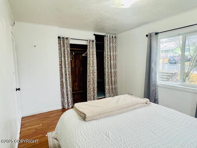 bedroom with a textured ceiling, a closet, wood finished floors, and baseboards