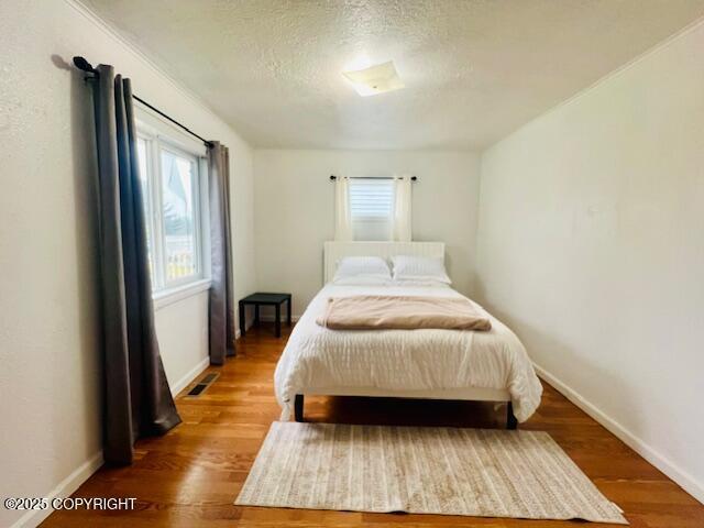 bedroom featuring visible vents, a textured ceiling, baseboards, and wood finished floors