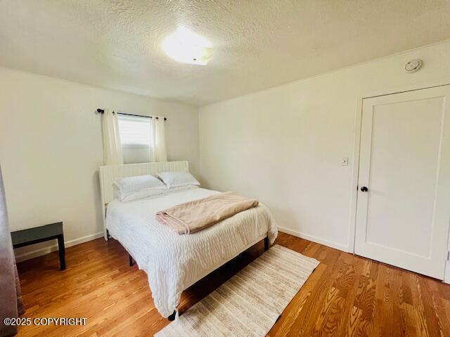 bedroom featuring a textured ceiling, baseboards, and light wood-style floors