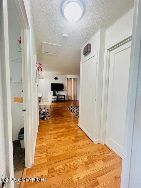 hallway featuring light wood-style floors, attic access, and a textured ceiling