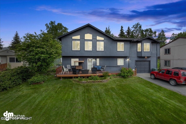 back of house featuring an attached garage, driveway, a lawn, and a wooden deck