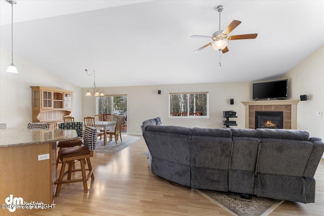 living room with a ceiling fan, a tile fireplace, vaulted ceiling, and light wood finished floors