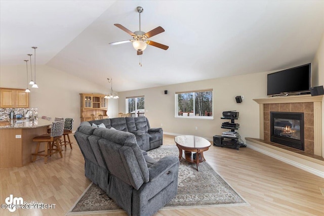 living room with lofted ceiling, light wood-type flooring, a fireplace, and ceiling fan with notable chandelier