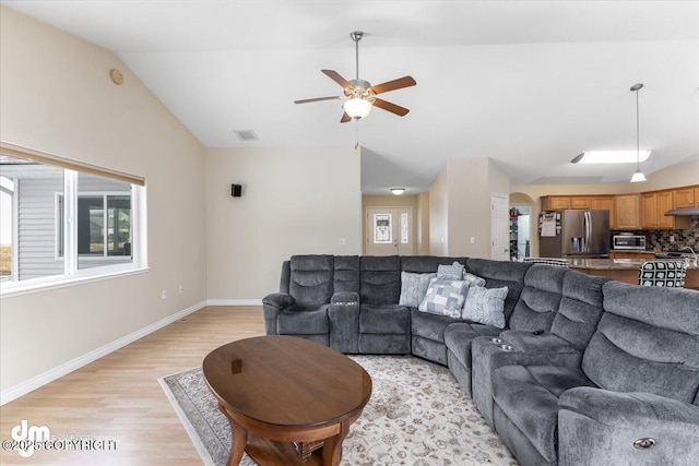 living area with visible vents, baseboards, ceiling fan, light wood-style flooring, and vaulted ceiling