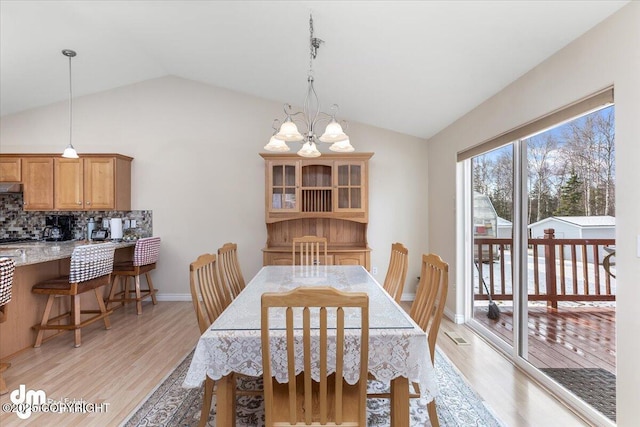 dining space featuring light wood finished floors, baseboards, a chandelier, and vaulted ceiling