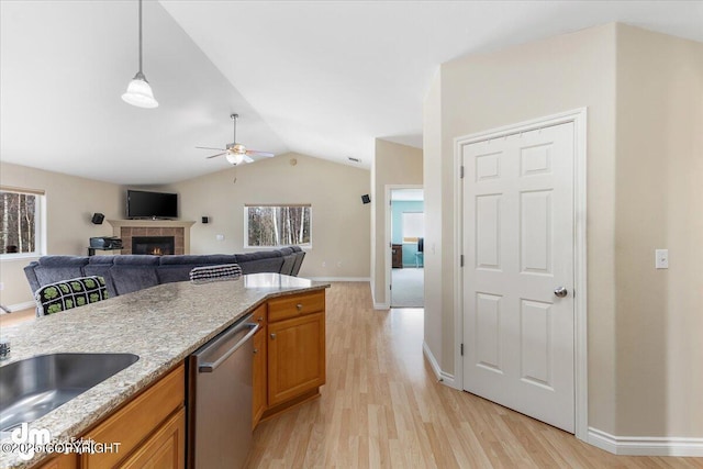 kitchen featuring lofted ceiling, a tile fireplace, stainless steel dishwasher, light wood-type flooring, and brown cabinets