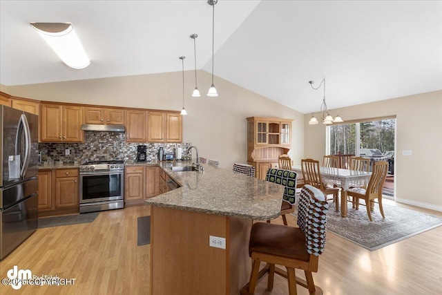 kitchen featuring appliances with stainless steel finishes, a peninsula, under cabinet range hood, a kitchen bar, and a sink