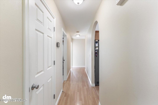 hallway with arched walkways, light wood finished floors, and baseboards