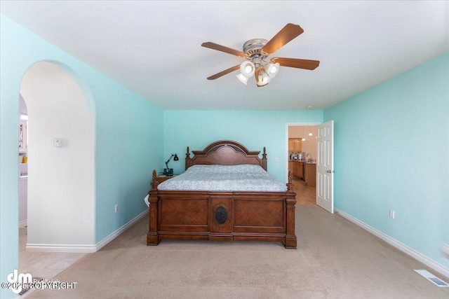 bedroom with arched walkways, visible vents, light carpet, ceiling fan, and baseboards