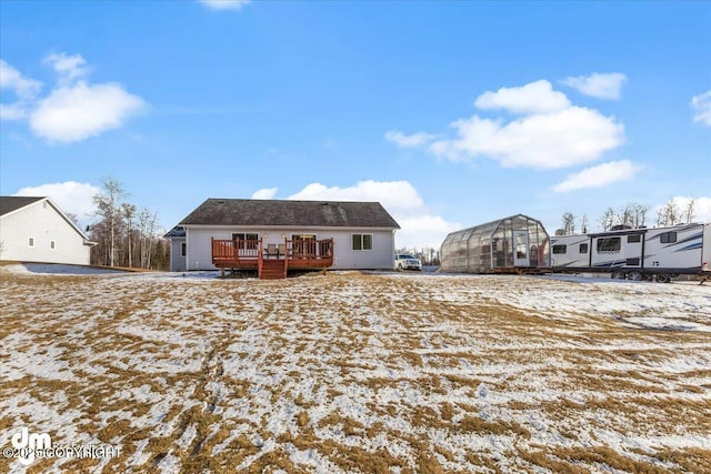 snow covered rear of property with a greenhouse, a wooden deck, and an outbuilding