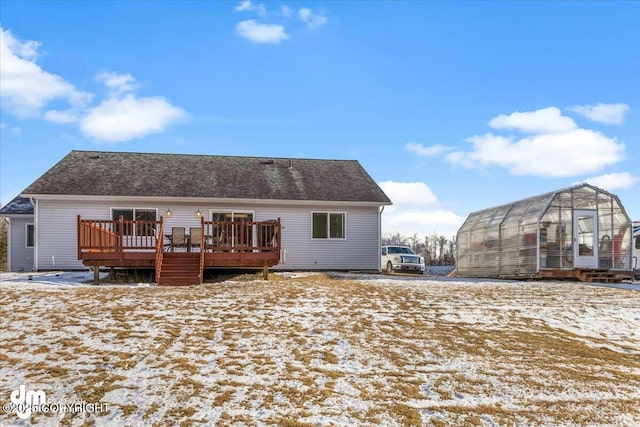 snow covered rear of property featuring an outbuilding, a greenhouse, and a wooden deck