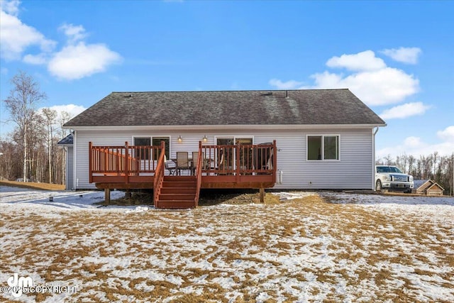 snow covered rear of property featuring a deck and a shingled roof