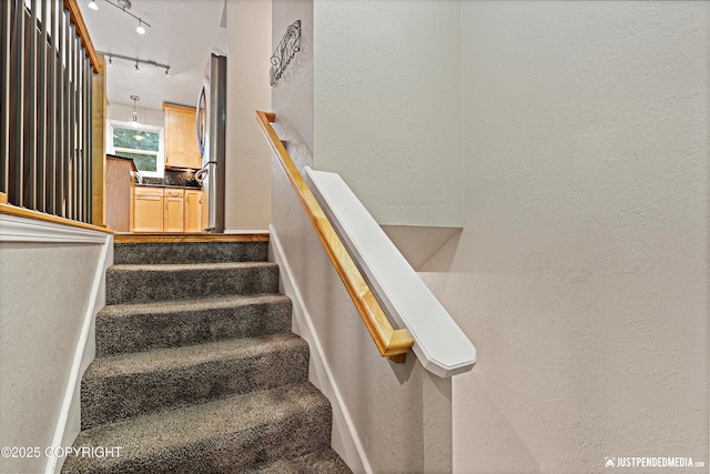 stairway featuring rail lighting and a textured wall