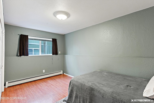 bedroom with a baseboard radiator, a textured ceiling, and wood finished floors