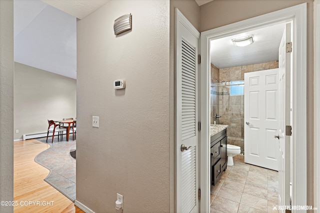 corridor with a baseboard heating unit and a textured wall