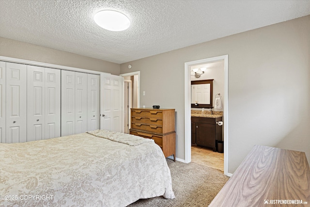 bedroom featuring a closet, light colored carpet, a textured ceiling, ensuite bath, and baseboards