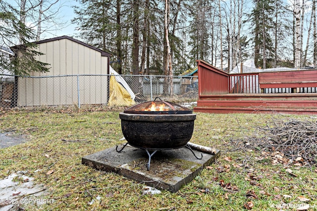 view of yard with a storage unit, fence, a deck, an outdoor structure, and a fire pit