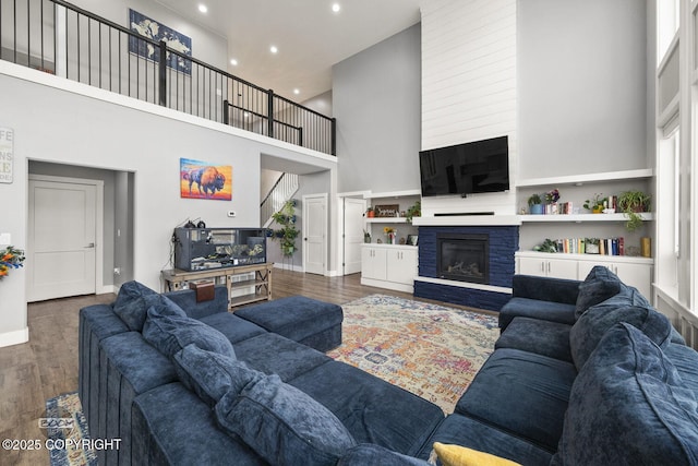 living room featuring a fireplace, recessed lighting, a towering ceiling, wood finished floors, and baseboards