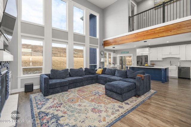 living room with a stone fireplace, a high ceiling, wood finished floors, and baseboards