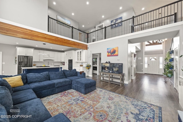 living room featuring a high ceiling, baseboards, dark wood finished floors, and recessed lighting