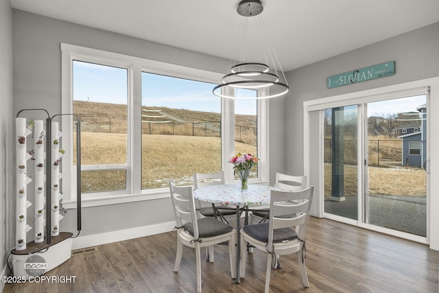 dining room featuring visible vents, plenty of natural light, baseboards, and wood finished floors