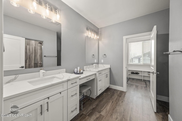 bathroom with wood finished floors, two vanities, a sink, and baseboards