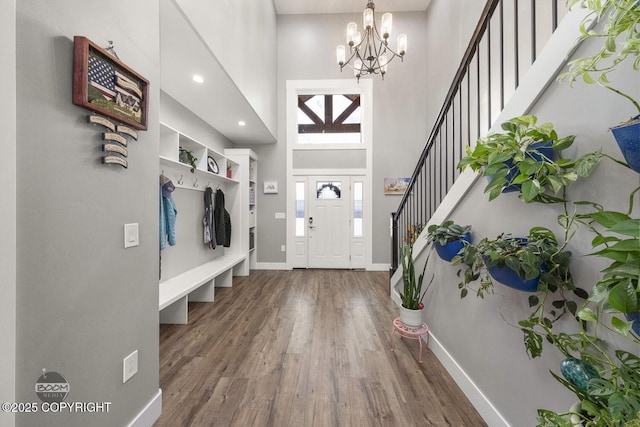 foyer entrance featuring baseboards, a towering ceiling, wood finished floors, an inviting chandelier, and stairs