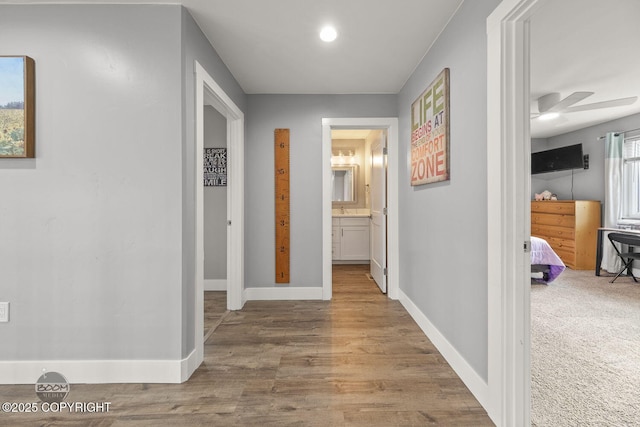 hallway featuring a sink, baseboards, and wood finished floors