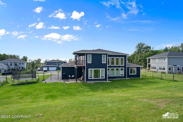 rear view of property featuring a patio area, a trampoline, fence, and a lawn