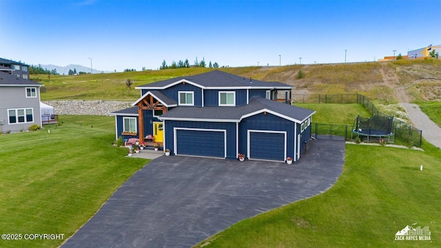 view of front of property with aphalt driveway, a trampoline, fence, a front lawn, and board and batten siding