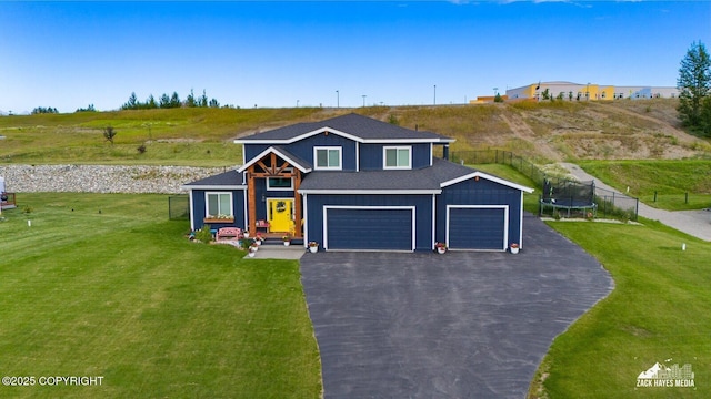 view of front of house featuring driveway, a shingled roof, a trampoline, fence, and a front lawn