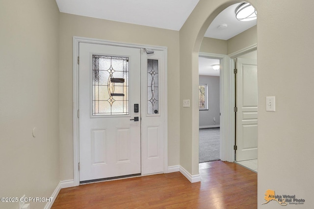 entryway featuring baseboards, arched walkways, and wood finished floors