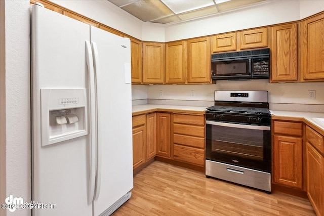 kitchen featuring stainless steel gas range oven, black microwave, light countertops, white refrigerator with ice dispenser, and light wood-style floors