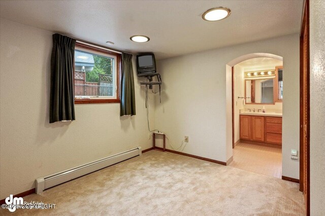 unfurnished bedroom with a baseboard heating unit, baseboards, light colored carpet, arched walkways, and ensuite bath