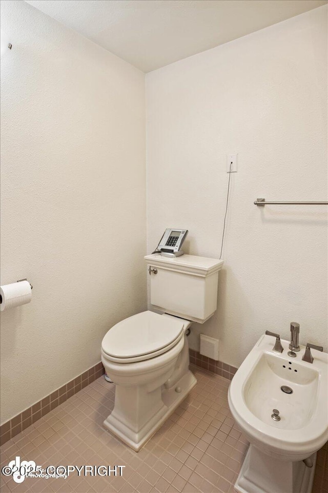 bathroom featuring tile patterned floors, toilet, a bidet, and baseboards