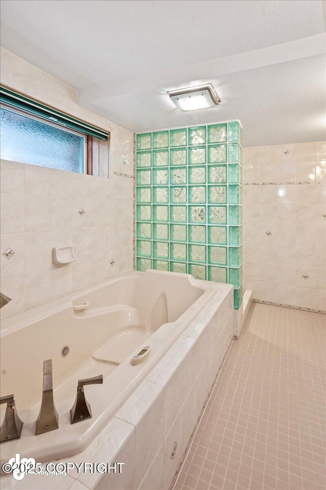 bathroom with tile walls, tile patterned floors, a whirlpool tub, and a textured ceiling