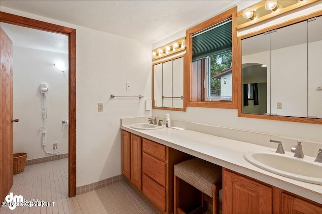 full bath with double vanity, tile patterned floors, baseboards, and a sink