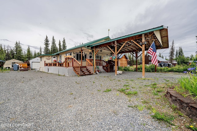 view of front of property with gravel driveway, a detached garage, metal roof, a deck, and an outdoor structure