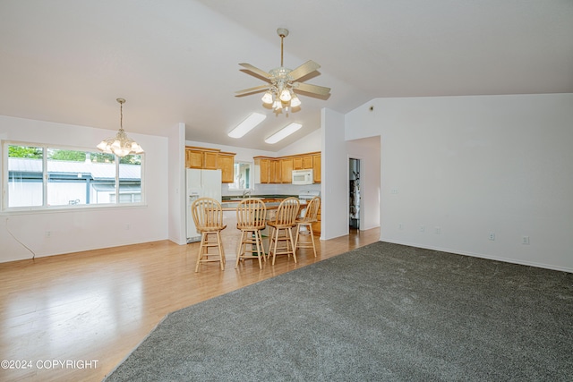 kitchen featuring ceiling fan with notable chandelier, white appliances, a breakfast bar, open floor plan, and vaulted ceiling