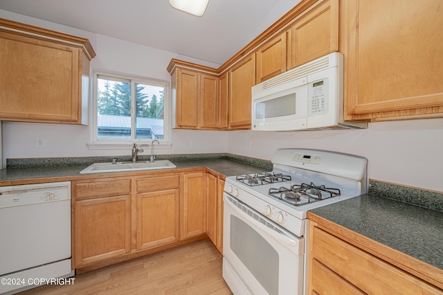 kitchen featuring light wood-style floors, dark countertops, white appliances, and a sink